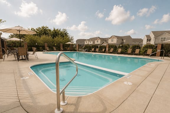 A swimming pool surrounded by a concrete deck and patio furniture.