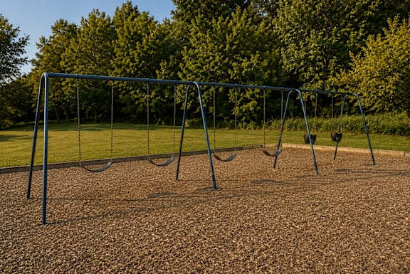 A swing set in a playground with a brown ground and trees in the background.
