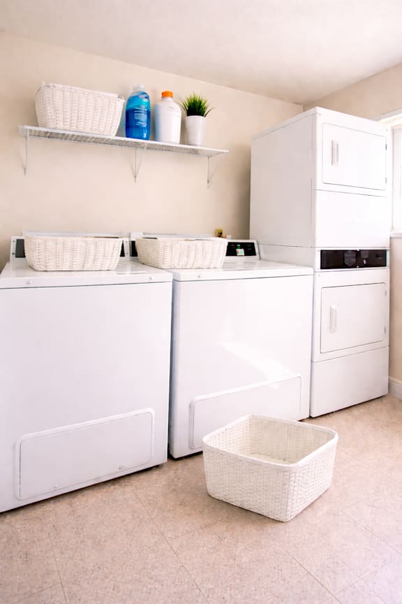A white kitchen with a white fridge, white cupboards and white baskets.