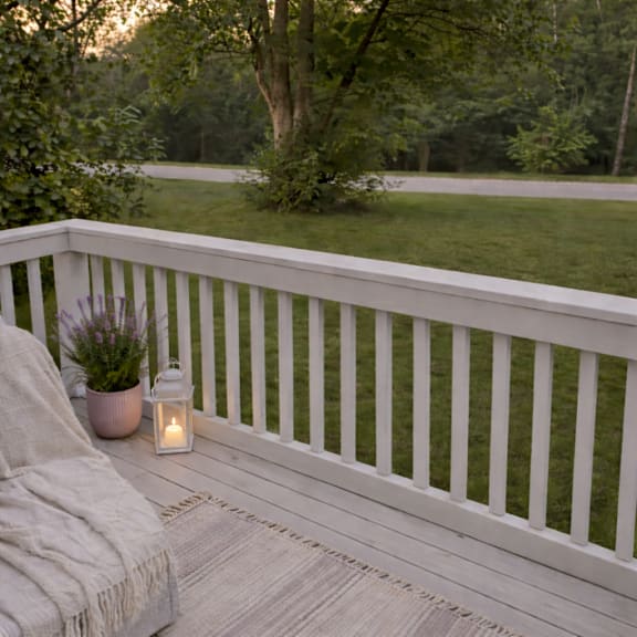 A white railing with a lit candle and a potted plant on a wooden floor.