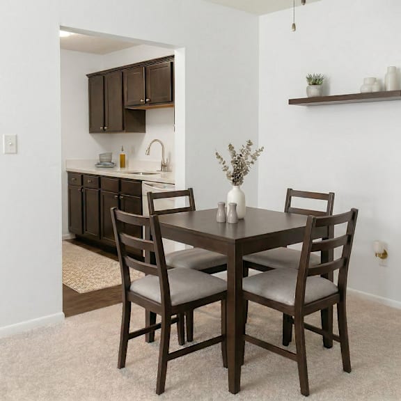 A brown wooden dining table with four chairs and a vase with flowers on it.