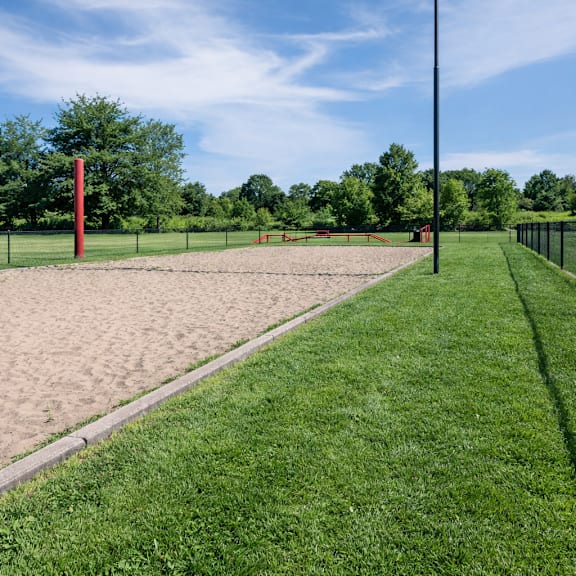A red pole stands in a sandy area next to a green grassy area.