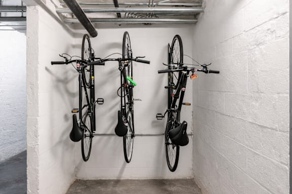 Three bicycles are parked side by side in a white-walled bike rack.