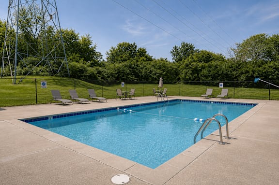 A large swimming pool surrounded by a fence and lounge chairs.