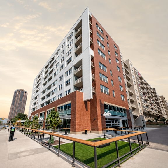 A modern multi-story building with a red brick facade and a balcony with a wooden railing.