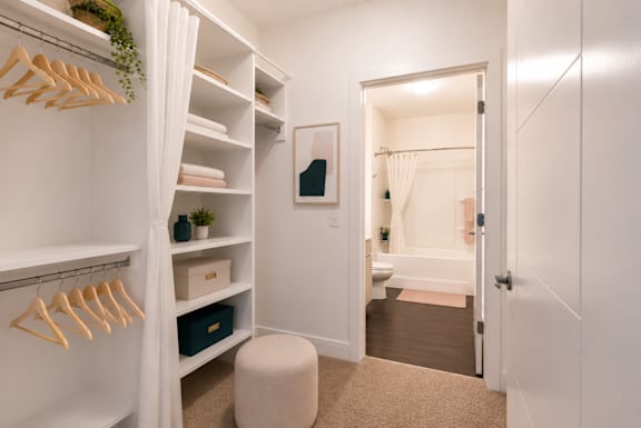A white closet with a mirror and a doorway leading to a bathroom.