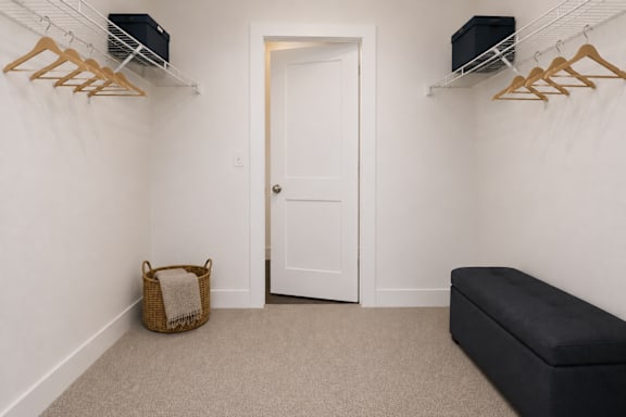 A room with a white door, a bench, and a wall-mounted shelf with clothes hangers.