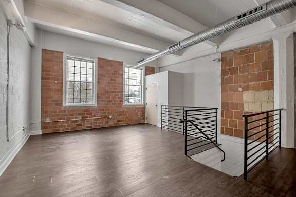 Industrial loft space with exposed brick and metal stair railing at The Lofts at Elk Terminal Apartments, Buffalo, NY