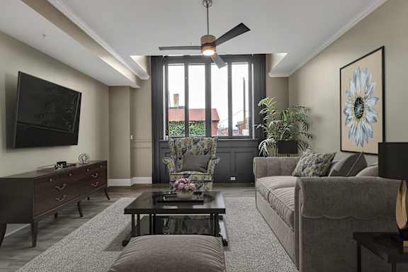 A living room with a grey couch, a coffee table, and a flat screen TV mounted on the wall.