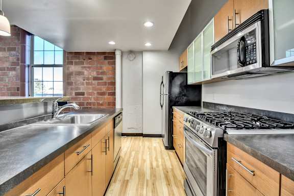 Galley kitchen with exposed brick and stainless appliances at The Lofts at Elk Terminal Apartments, Buffalo, New York