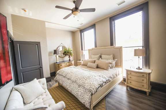 A bedroom with a large bed, a ceiling fan, and a window with blinds.