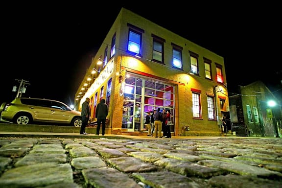 A group of people are standing outside a building with brightly lit window at The Lofts at Elk Terminal Apartments, Buffalo, NY