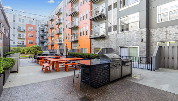an outdoor patio with picnic tables and a grill in front of an apartment building at Bakery Living in Pittsburgh, PA 15206
