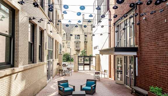 a courtyard with blue chairs and a red brick building in the background at Walnut on Highland, Pennsylvania 15206