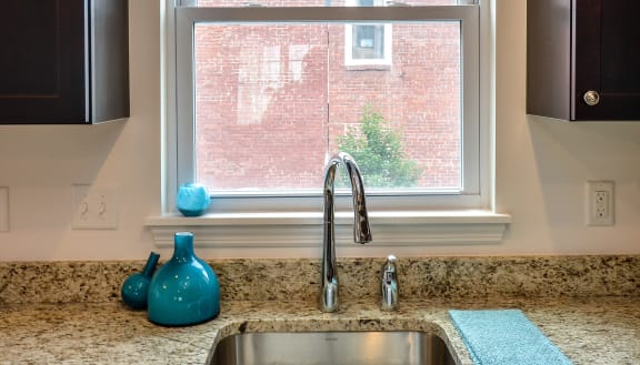 a kitchen sink in front of a window with a red brick building in the background