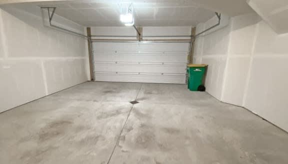A white garage with a green trash can and a white wall.