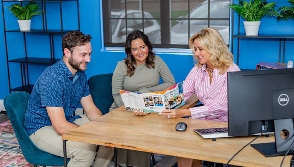 Three people are sitting at a table with a computer and a magazine. at Highland Village, 15229