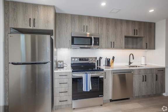 A modern kitchen with a stainless steel refrigerator, microwave, oven, and sink.