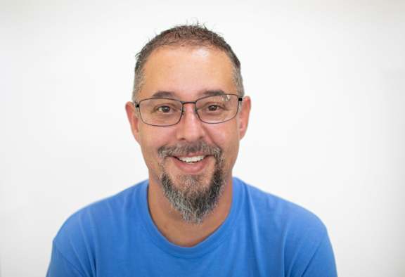 A man with glasses and a blue shirt is smiling.