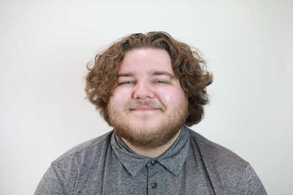 A man with curly hair and a beard is smiling.