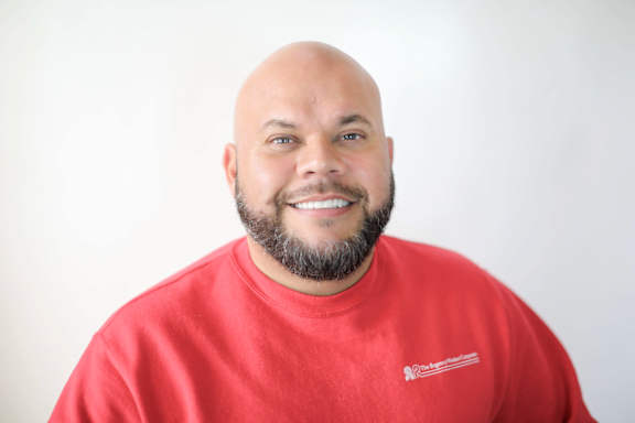 A man with a beard wearing a red shirt with a logo on it.