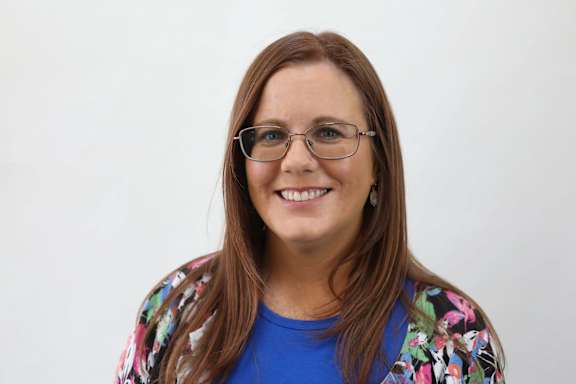 A woman with glasses and a floral shirt is smiling.