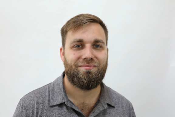 A man with a beard is wearing a grey shirt.