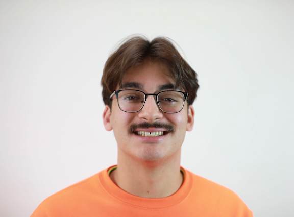 A man with glasses and a mustache wearing an orange shirt.