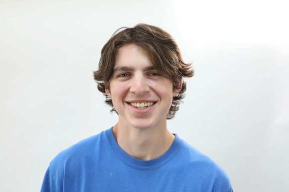 A young man with brown hair and a blue shirt is smiling.