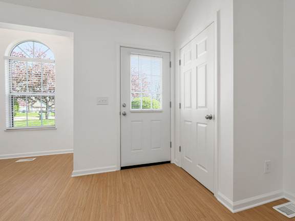 A room with white walls and a wooden floor with a window and three doors.