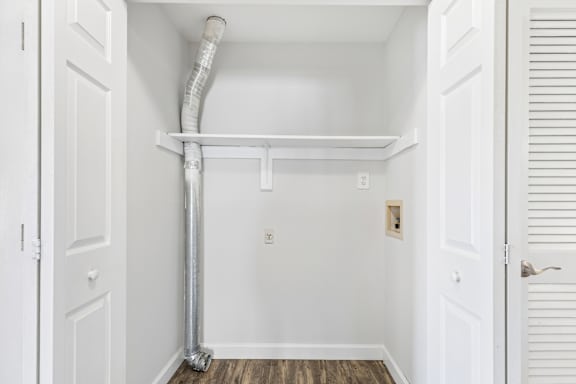 A white door is open to a room with a white wall and a white pipe running along the wall.