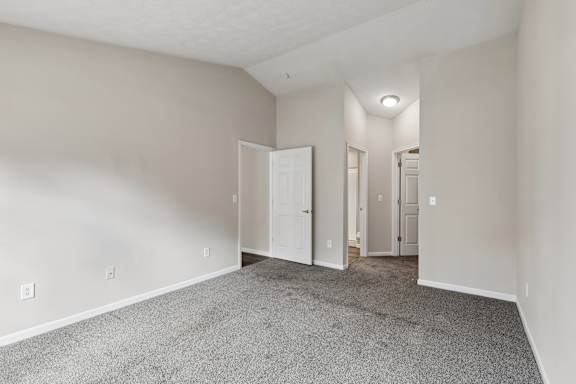A room with carpeted floor and white walls with three doors.