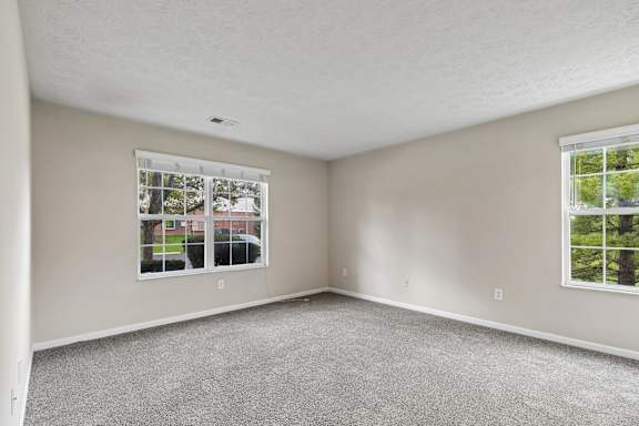 A room with a carpeted floor and two windows.