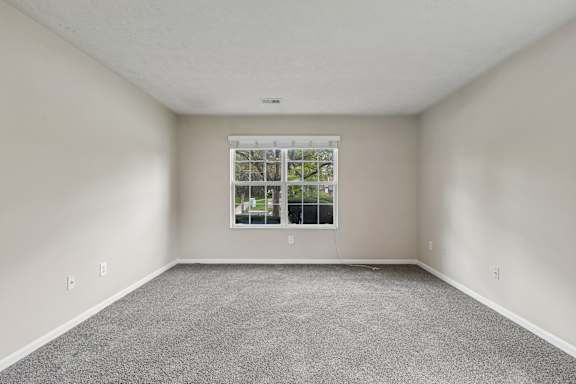 A room with a carpeted floor and a window showing a view of trees and a building.