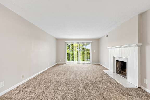 A spacious living room with a fireplace and a sliding glass door leading to a balcony.