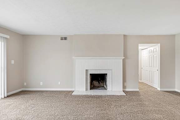 A white fireplace in a room with beige walls and carpet.