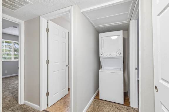 A white refrigerator is in a narrow hallway.