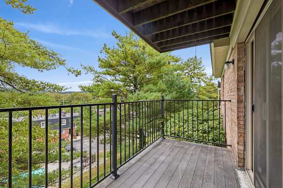 A balcony with a black railing and a view of a street and trees.