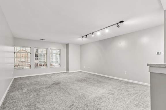 A spacious room with grey carpeting and a window with blinds.