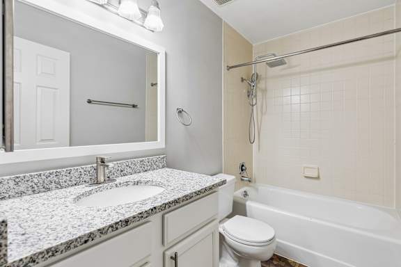 A white bathroom with a marble countertop and a white toilet.