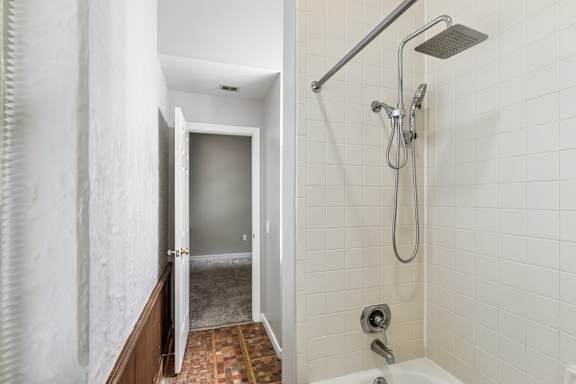 A bathroom with a shower and a doorway leading to a hallway.