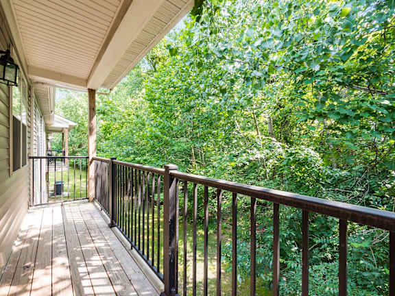 A wooden deck with a railing overlooks a lush green forest. at River View at Bexley Apartments, Ohio