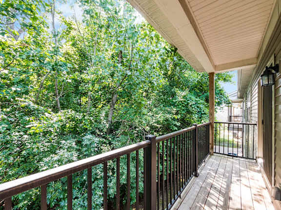 A balcony with a railing overlooks a lush green forest. at River View at Bexley Apartments, Ohio, 43209