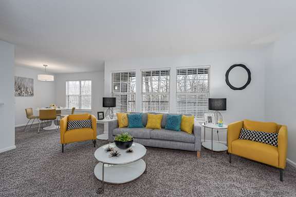 A living room with a grey couch, yellow chairs, and a white coffee table at Indian Lookout Apartments, West Carrollton, 45449