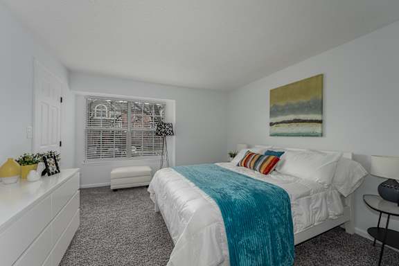 A bedroom with a bed, nightstand, and a painting on the wall at Indian Lookout Apartments, West Carrollton, OH