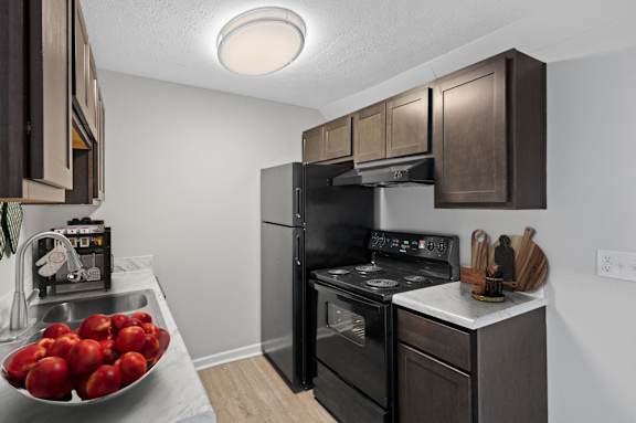 A kitchen with a black oven and a bowl of red apples on the counter.