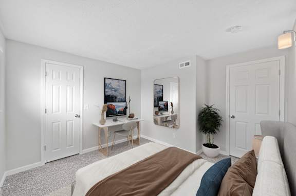 A bedroom with a bed, a table with a vase and a picture frame, and a potted plant.