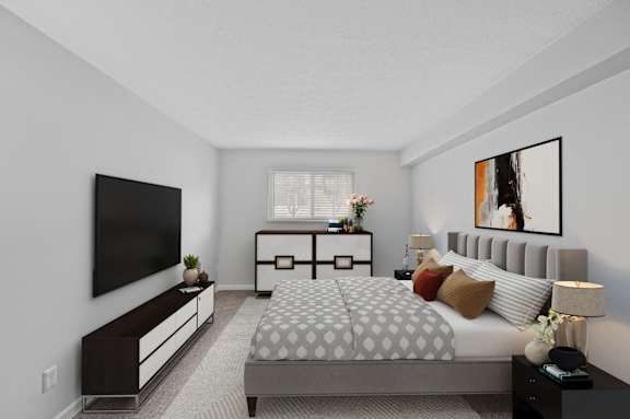 A bedroom with a large bed, a television, and a nightstand with a lamp.