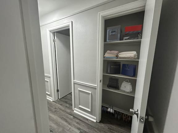 A white door is open to a hallway with a shelf underneath it.