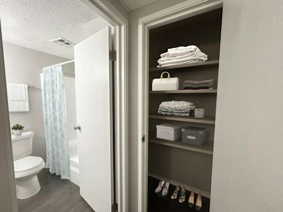 A bathroom with a toilet, a shower curtain, and a cabinet with towels and shoes.